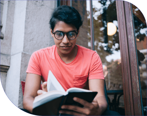 Student in glasses sits outside a glass door and reads.