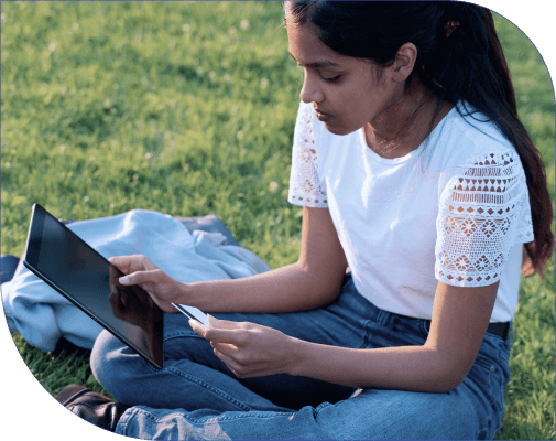 Indian girl using a tablet on the grass.