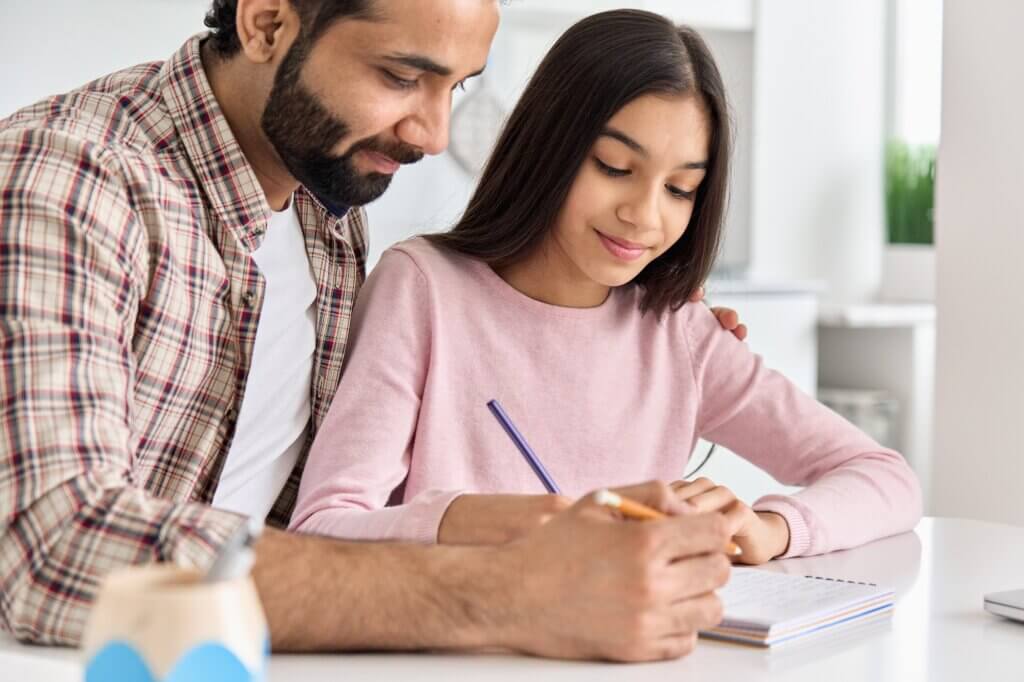 Happy indian father helping school kid teen daughter learning at home.