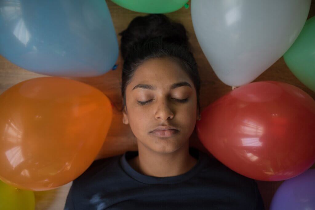 Child laying down amongst balloons, eyes closed.