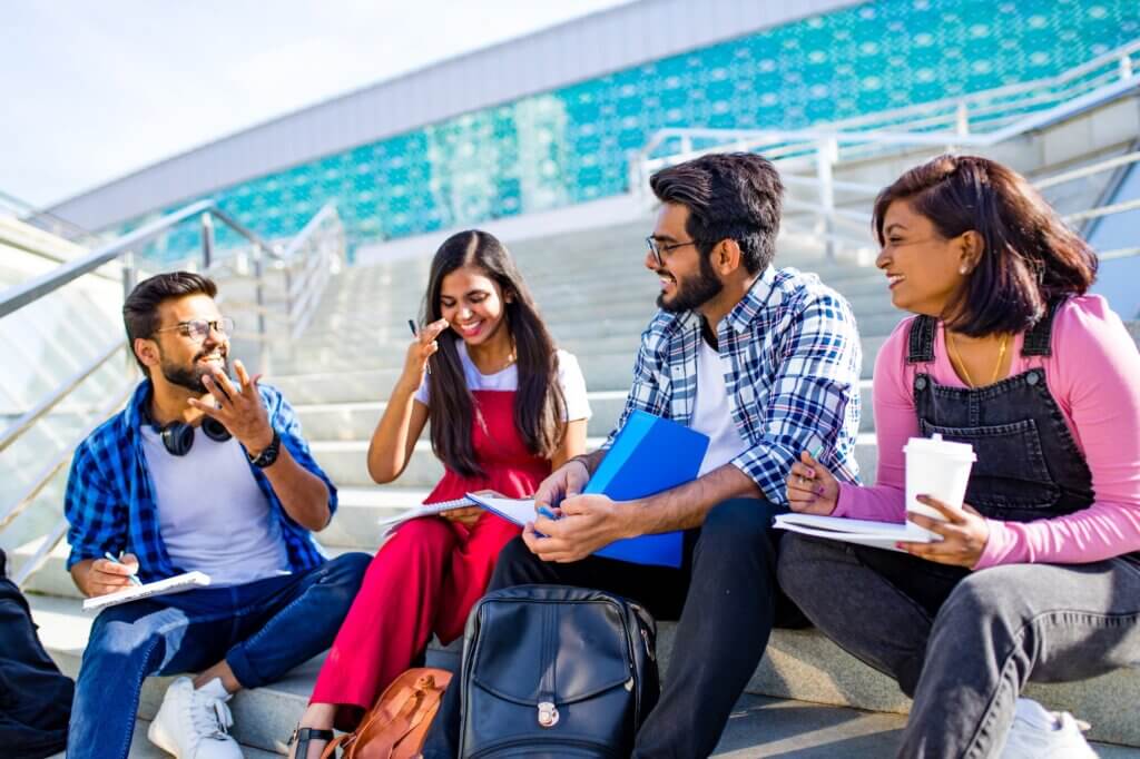 indian friends sitting on stairs outdoors with copybooks .